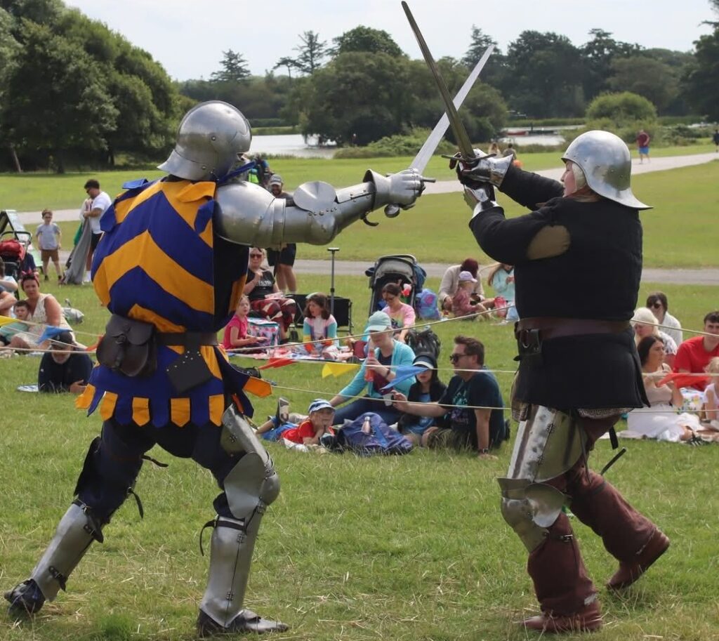A knight and squire fight each other with swords before the public